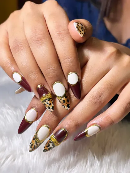 For the client who dares to be different. This set features sharp, stiletto extensions with a mix of deep burgundy, hand-painted leopard print, and a unique white 'negative space' design framed in gold.