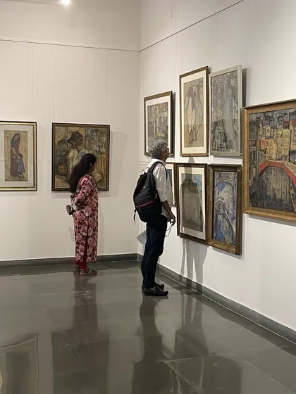 Two visitors contemplating a wall of Vidya Bhushan's paintings, which range from portraits to cityscapes.