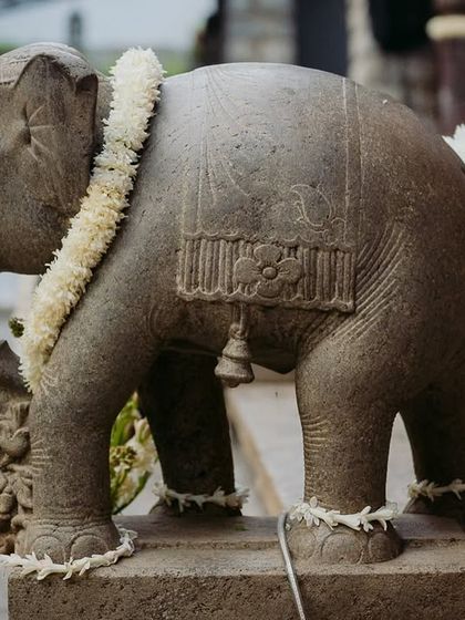 A stone elephant statue adorned with a fresh flower garland, a simple yet beautiful touch of tradition.