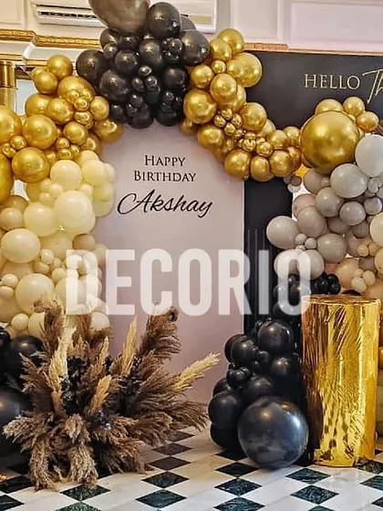 An elegant 'Hello Thirty' birthday backdrop designed for a sophisticated celebration. The decor features a stylish black, gold, and white balloon arch framing a personalized backdrop, complemented by pampas grass arrangements and a gold pedestal for a chic, modern look.
