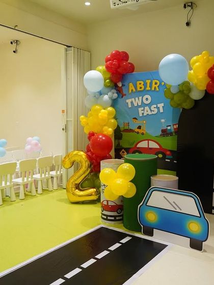 Part of a "Two Fast" car-themed party, this area includes a road-themed floor mat, a balloon arch, and car cutouts for the kids' seating area.