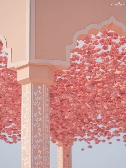 A close-up of a hand-painted pillar and the canopy of the mandap, which is densely covered in pink carnations to create a stunning floral ceiling.