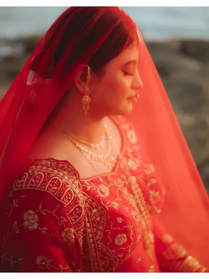 A close-up of the bride in her red veil, bathed in the warm glow of the sun. This shot highlights the delicate embroidery of her outfit and her serene expression.