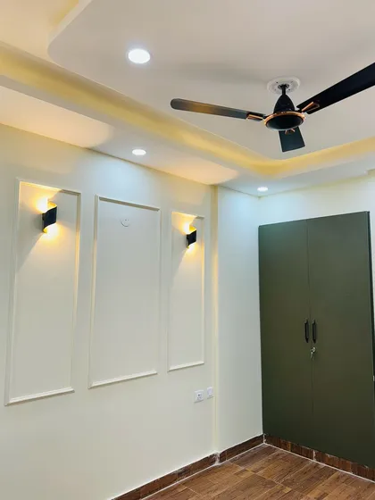 This bedroom features a dark green wardrobe that pairs beautifully with the simple POP moulding and wall-mounted lights.