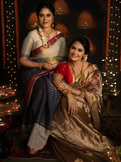Shubha Deepawali! Two women in elegant sarees share a diya, their faces glowing in the warm light of the festival.