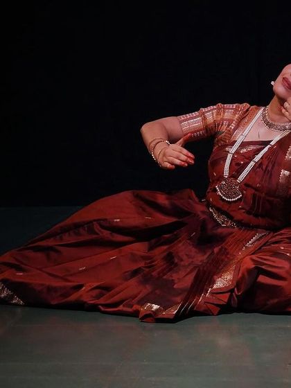 A graceful pose from 'Rasayatra', showcasing the dancer's control and artistry. The lighting highlights the rich colours of her costume against the dark backdrop.