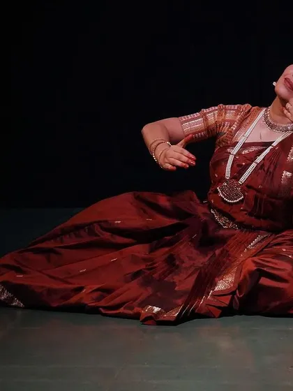 A graceful pose from 'Rasayatra', showcasing the dancer's control and artistry. The lighting highlights the rich colours of her costume against the dark backdrop.