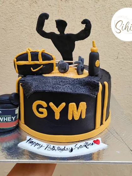 A powerful gym-themed cake for a fitness enthusiast. This black and yellow cake is loaded with fondant details like a whey protein tub, dumbbells, and a bodybuilder silhouette.