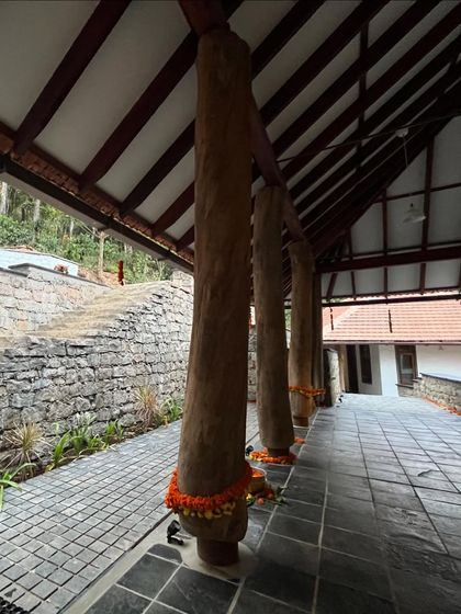 The entrance veranda of the Coorg house, featuring massive reclaimed timber pillars that ground the building and speak to the local vernacular style.