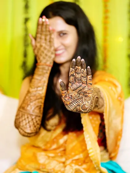 A creative shot focusing on the detailed palm of the bride's henna, with her smiling face peeking from behind.