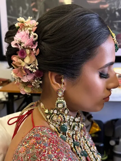 A side view of a floral bridal bun, showing how the arrangement of pink hydrangeas frames the face and complements the bride's elaborate jewelry.