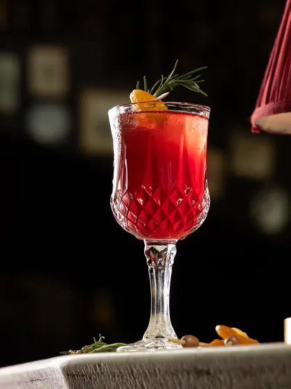 A symphony of flavors in every glass. This deep red cocktail, garnished with rosemary and orange, is a perfect example of the indulgent, handcrafted creations from our bar.