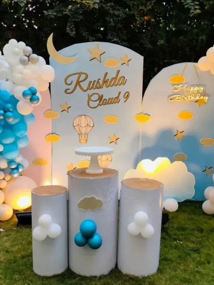 This dreamy 'Cloud 9' themed birthday was set up outdoors, featuring soft blue and white tones with gold accents. The decor includes custom cloud-shaped props, a personalized name backdrop, and gentle lighting to create a serene and magical atmosphere.
