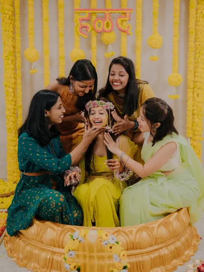 The bride's friends playfully apply Haldi to her face, her laughter capturing the fun and festive spirit of the ceremony.