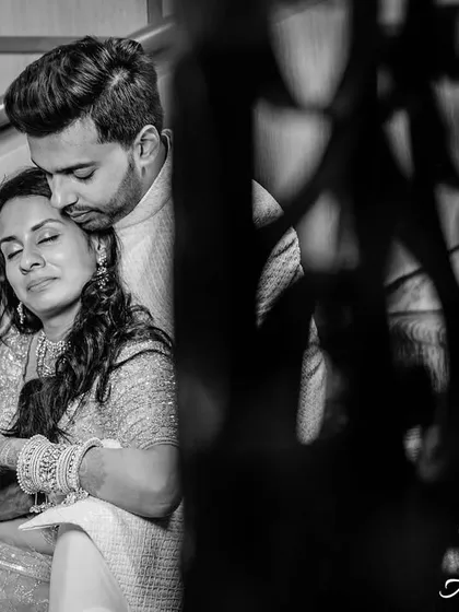 A beautifully framed black and white portrait of a couple sharing a quiet moment on a staircase. The foreground element adds depth and a sense of intimacy to the scene.