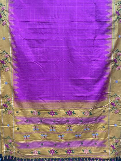 A full view of the vibrant purple Kanjeevaram silk saree with a rich gold border. The pallu and border are decorated with colorful Kamal Kadai embroidery, featuring floral and butterfly motifs that tell a story.