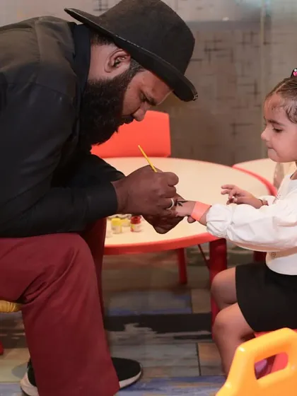 A close-up of our artist carefully painting a design on a child's hand. It's a calm and creative activity amidst the party excitement.