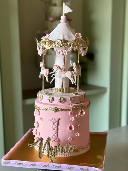 A fairytale spinning to life for a little one's first birthday. This two-tier carousel cake, with its delicate pink fondant, handcrafted horses, and intricate gold details, is a perfect example of the whimsical magic we love to create for childhood celebrations.