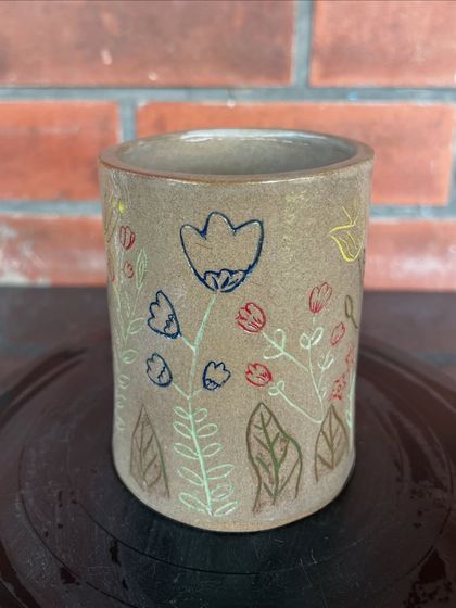 A lovely tumbler-style vase with colorful, child-like flowers etched and painted on the surface. This was made by a student and shows so much personality.