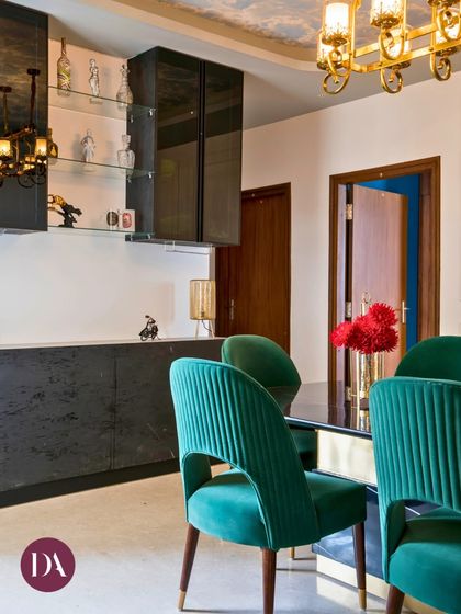 The rich, emerald green velvet of these dining chairs adds a luxurious texture to the room. Paired with a sleek black dining table and a modern bar unit, the space is designed for sophisticated entertaining.