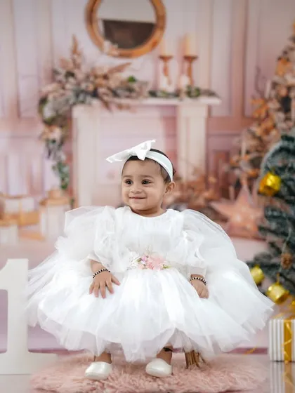 A beautiful, serene portrait of the little one in her fluffy white dress, surrounded by Christmas trees and presents.
