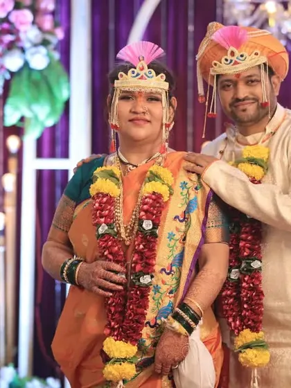A classic portrait of the couple in their vibrant orange and cream wedding attire, showcasing the beauty of Maharashtrian bridal and groom wear.