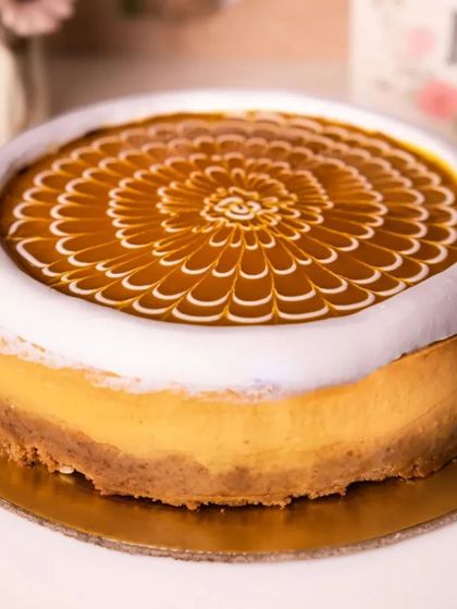 An elegant baked cheesecake with a beautiful feathered caramel design on top.