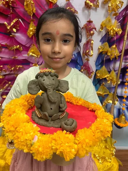 This student proudly holds up her eco-friendly Ganesha, sculpted with care and ready for worship.