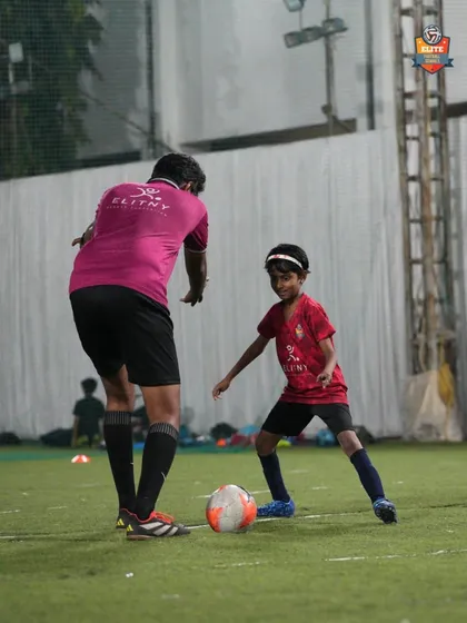 A coach provides one-on-one guidance to a young player, correcting her stance and technique to improve her dribbling skills.