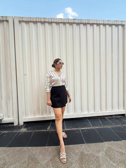 A full view of the satin shirt styled with a black skort. This is a chic boss babe look that is perfect for a smart casual setting. The vertical stripes are also very flattering.