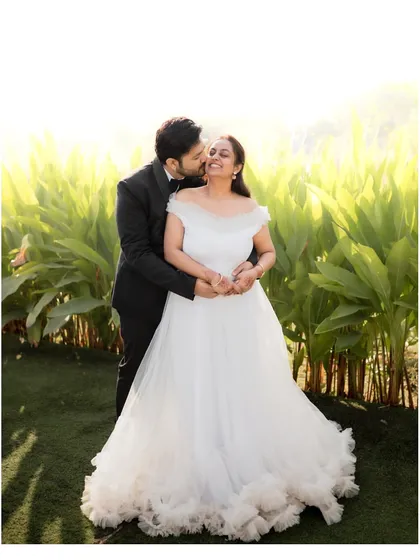 A sweet moment captured during a pre-wedding shoot, with the groom kissing the bride's cheek as they stand in a sunlit garden.