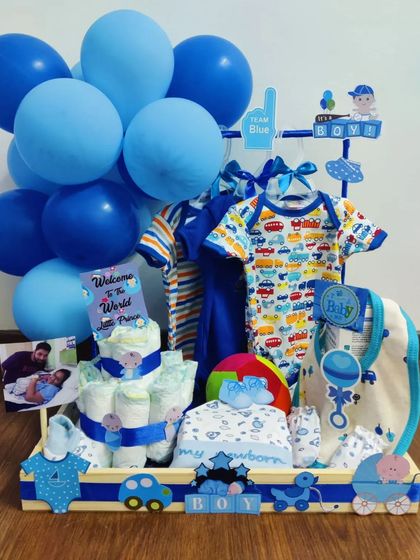 A classic 'It's a Boy' Jamna display, complete with a diaper cake, a variety of outfits, and personalized photo placements. The entire arrangement is coordinated in shades of blue to celebrate the little prince.