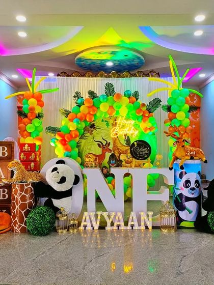 A vibrant jungle-themed first birthday party. This full-room decoration includes character cutouts of lions, pandas, and hippos, along with 'ONE' marquee letters and colorful balloon arrangements.