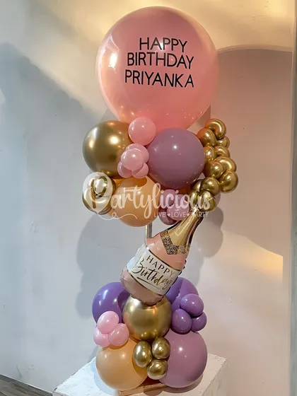 A chic and personalized birthday balloon bouquet. The custom "Happy Birthday Priyanka" message on the large balloon, paired with a mini champagne bottle and a stylish color palette, makes it a perfect gift.