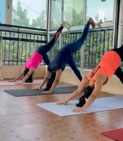 Students practicing Eka Pada Adho Mukha Svanasana (Three-Legged Downward-Facing Dog). This variation builds strength in the arms and shoulders while opening the hips.