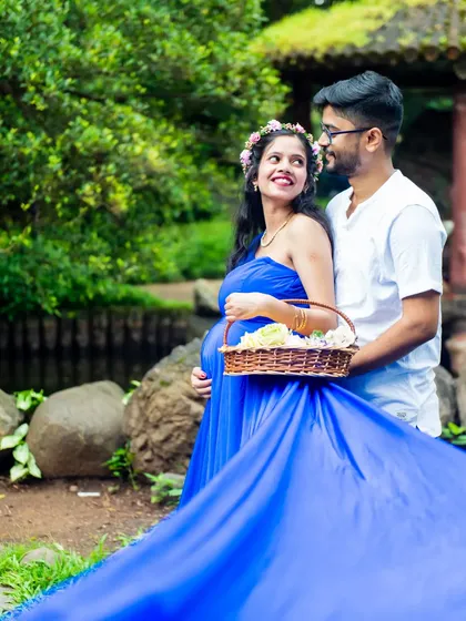 A fairytale moment in the garden. The mom-to-be looks radiant in a flowing blue gown, sharing a smile with her partner.
