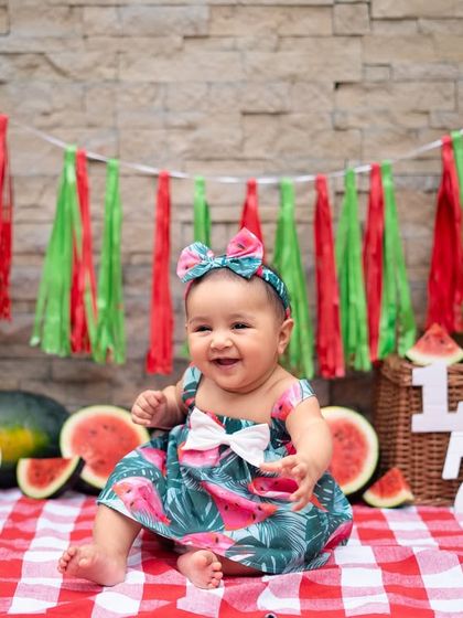 A happy smile from this six-month-old during her watermelon-themed shoot. The red and green decor and checkered picnic blanket create a perfect summer vibe.