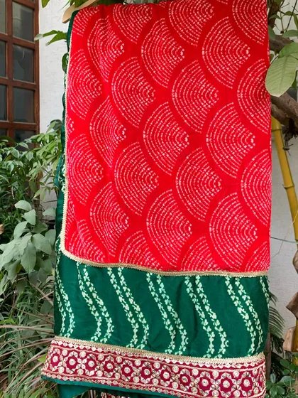 The vibrant red bandhani dupatta provides a stunning contrast to the green lehenga.