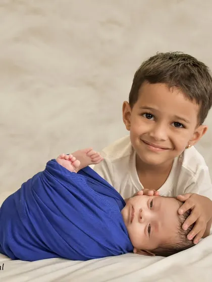 A heartwarming studio portrait of an older brother gently holding his newborn sibling, showcasing the beginning of a lifelong bond in a simple, tender moment.