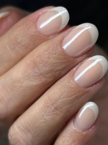 A beautiful reverse French or half-moon manicure. The design features a clean white crescent at the base of the nail, offering a modern and chic alternative to the classic French tip.