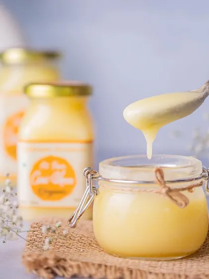 A close-up shot of pure A2 cow ghee, with a spoonful being lifted from the jar. The dripping ghee highlights its smooth, rich texture, which is a key selling point.