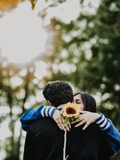 A creative and intimate shot where the couple embraces, with a single sunflower adding a touch of rustic charm. The bright backlighting creates a beautiful, dreamy halo effect around them.