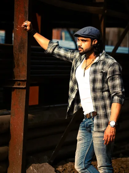 A different look in the same industrial setting. The plaid shirt and cap give off a more casual, rustic vibe against the metal structures.