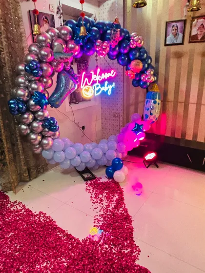 A 'Welcome Baby' ring decoration for a baby boy. This home setup features a circular balloon frame, a neon sign, and a pathway of red rose petals.