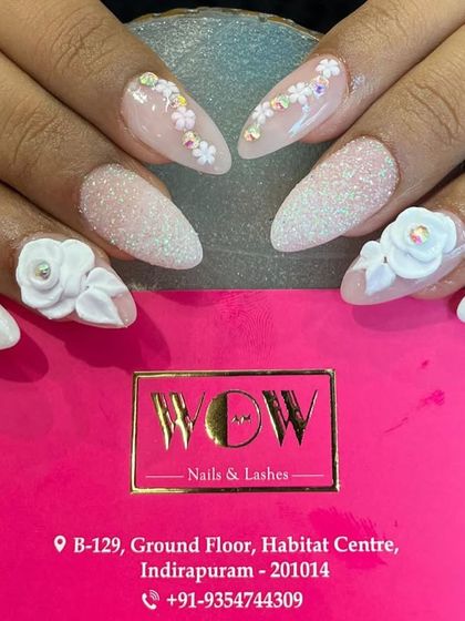A beautiful example of 3D nail art on long, almond-shaped extensions. This design features a white and pink ombré base with delicate, hand-sculpted 3D flowers and a textured glitter accent nail.