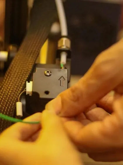 A close-up of hands feeding a new filament into the 3D printer's extruder. Learning to operate the machinery is a key part of our advanced 3D printing workshops.