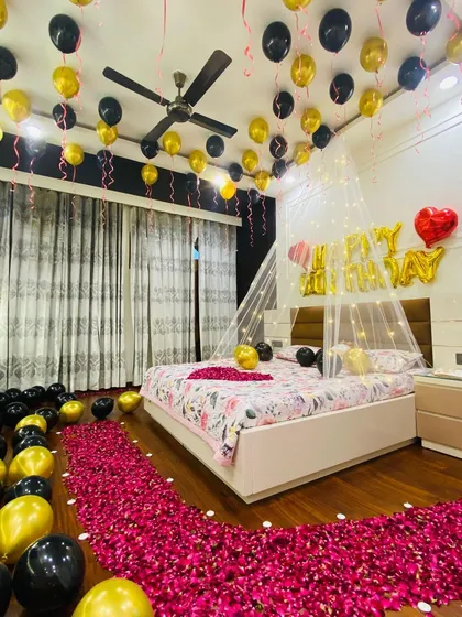 A full shot of the bedroom decorated for a birthday surprise. The pathway of rose petals leads from the door to the bed, creating a dramatic and romantic entrance.