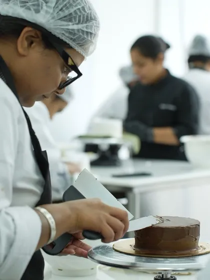 A student carefully applies chocolate ganache to her cake. Our classes provide a professional environment where you learn to work with different types of frostings and finishes, just like in a real bakery.