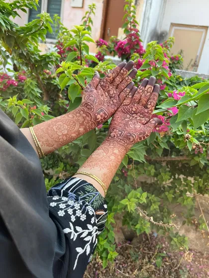 This showcases a complete bridal henna look, with intricate designs covering both palms and extending up the arms. The dark, uniform stain is exactly what you want for wedding photos.