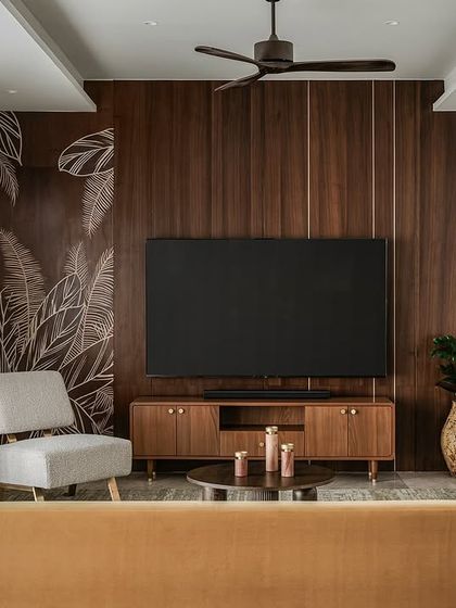 The informal living area at Tinted Tapestries, where we designed a custom ochre velvet sofa to bring a pop of warmth. The media wall is paneled in dark wood with a hand-painted botanical mural, creating a sophisticated yet relaxed atmosphere.
